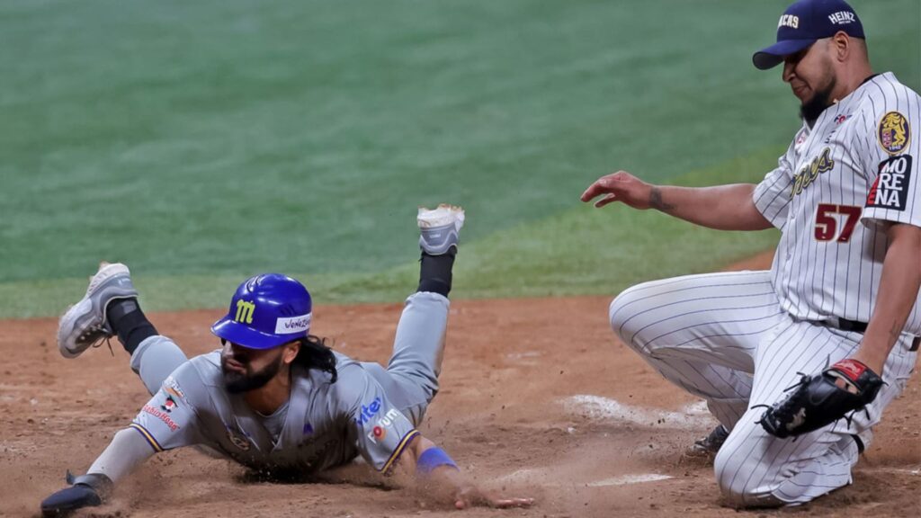 Miguel Aparicio de los Navegantes del Magallanes se desliza de cabeza en el plato mientras el lanzador de los Leones del Caracas, Mayckol Guaipe cubre la goma