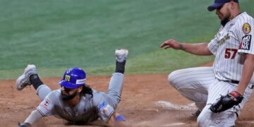 Miguel Aparicio de los Navegantes del Magallanes se desliza de cabeza en el plato mientras el lanzador de los Leones del Caracas, Mayckol Guaipe cubre la goma